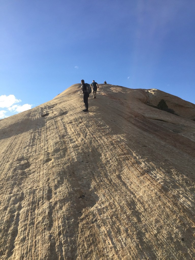 photo of three people walking up a steep, sheer rock cliff