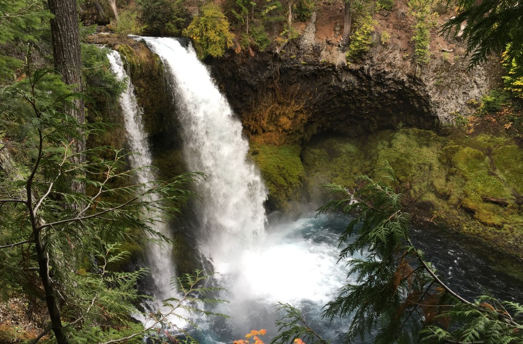 Waterfall gushes into a blue-green pool amidst lush greenery.