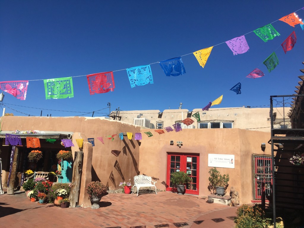 photo of one-story adobe buildings with brightly colored flags hanging against a blue sky