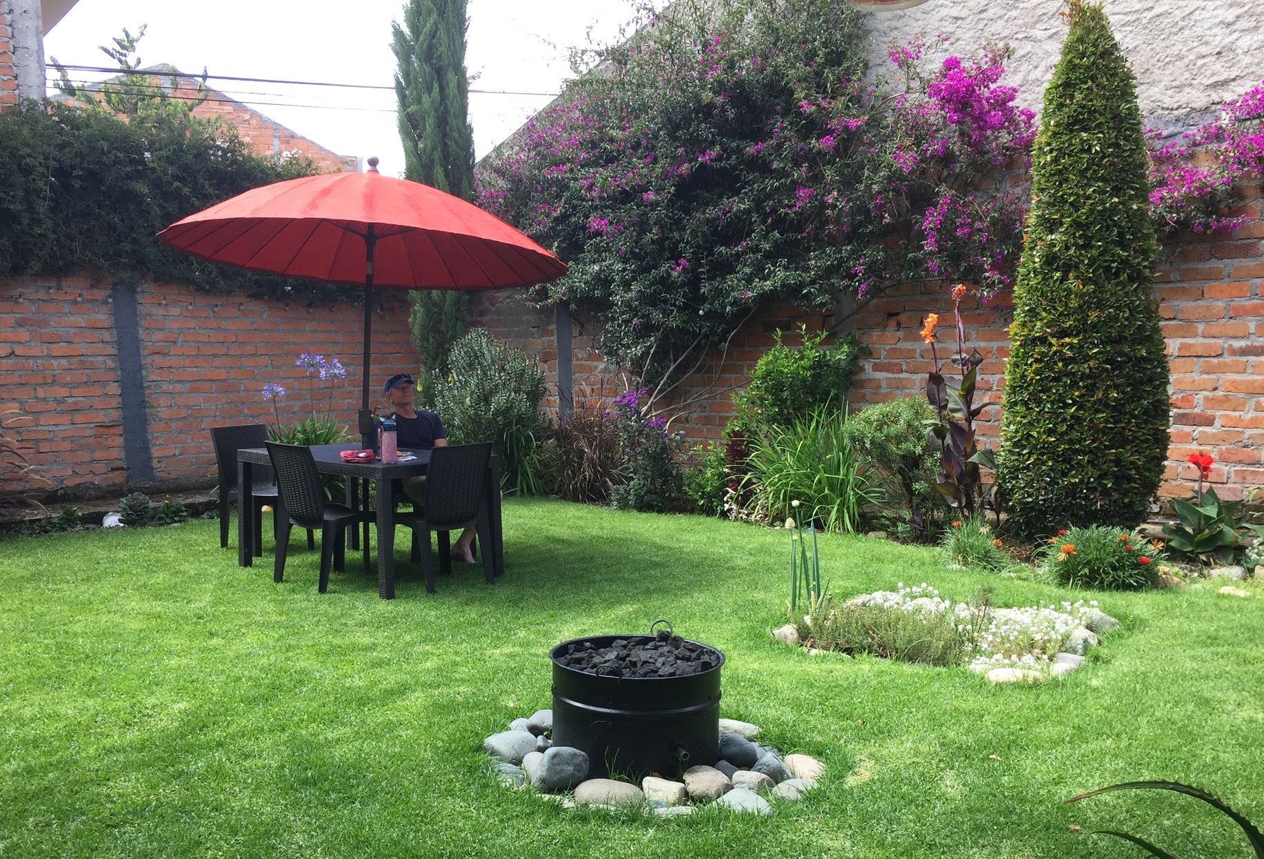 photo of a walled garden with flowering vines, green grass, and a picnic table with red umbrella