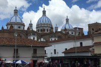 photo of three blue domes of a cathedral about a market plaza with white-walled buildings and red tile roofs