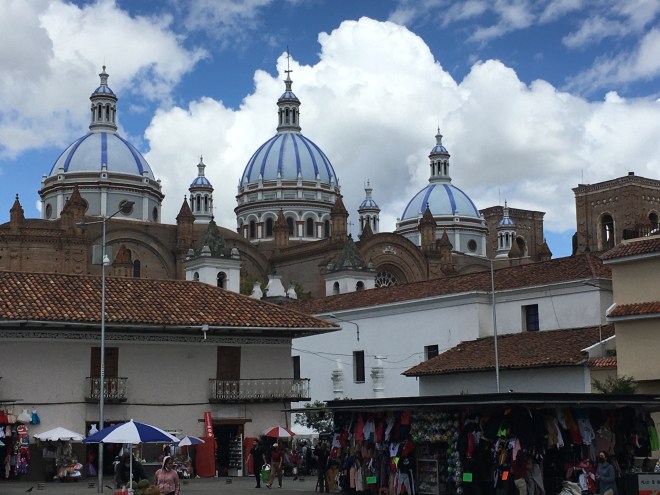 photo of three blue domes of a cathedral about a market plaza with white-walled buildings and red tile roofs