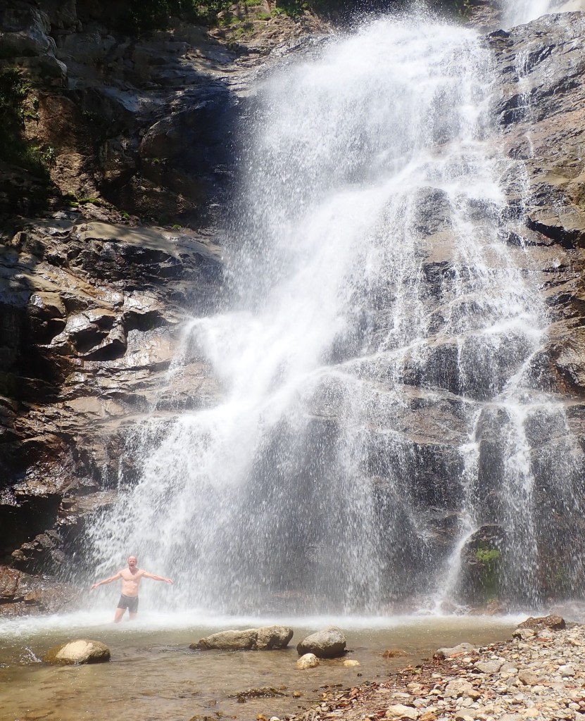 Photo of a high, white waterfall splashing down on a man standing at its base.
