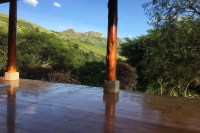 photo of a distant stone ridge, blue sky, green hills, taken from inside an open air, wood floor yoga studio with deep golden brown wooden pillars