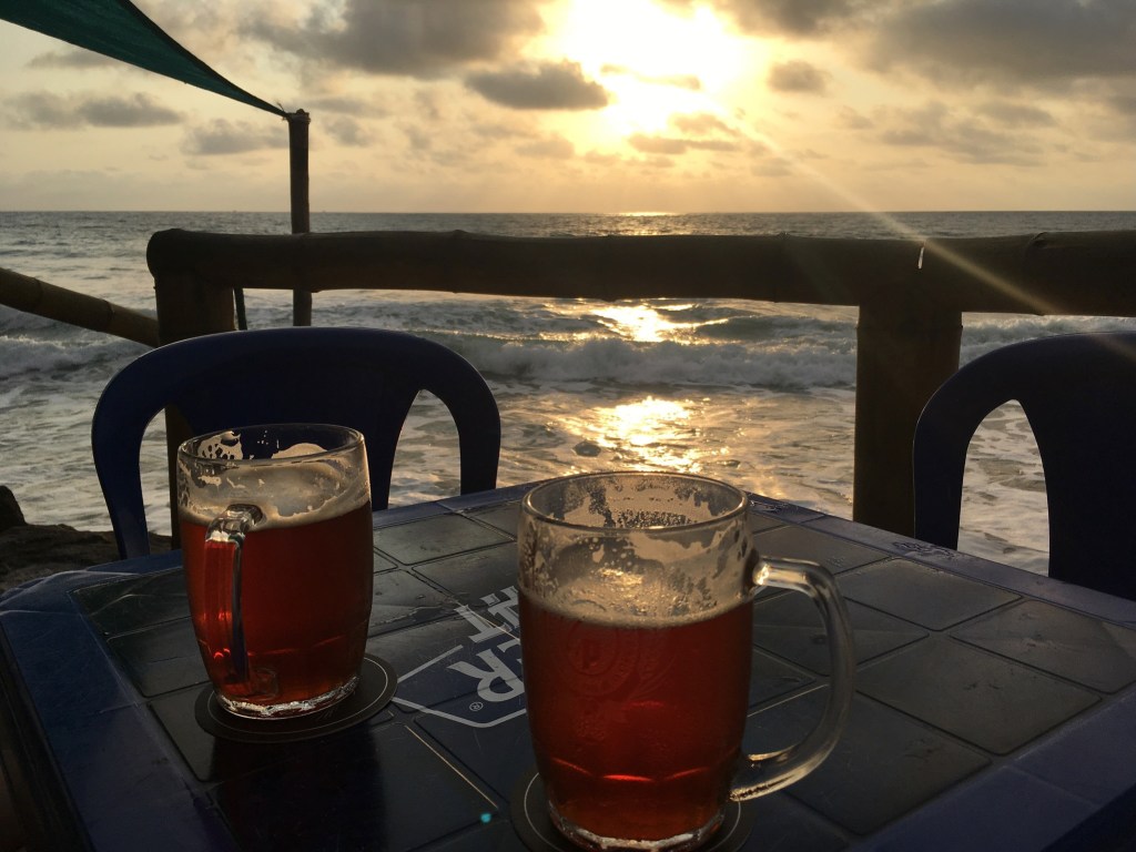 Photo of two beer mugs on a table overlooking ocean waves and a sunset.