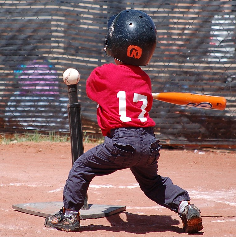 photo of a young child from the back swinging a bat at a baseball on a tee
