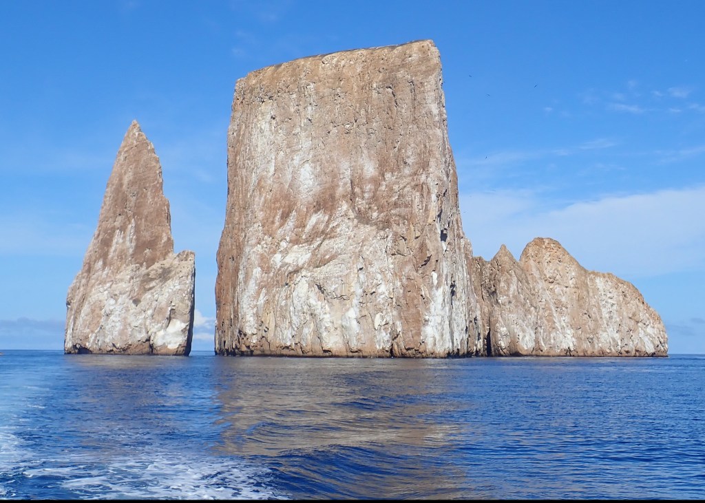 Photo of two towers of rock separated by a small channel, with blue skies above and blue seas below.
