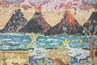 photo of a ceramic mosaic of four volcanoes spewing lava behind a sea with waves, a sandy beach, and two tortoises being ridden by white birds.
