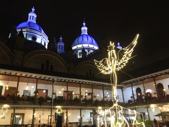 Photo of blue church domes above a courtyard with white lights in the shape of an angel.