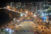 photo of a street at night beside a harbor, crowded with cars and people, winding around a roundabout with buildings and bright lights