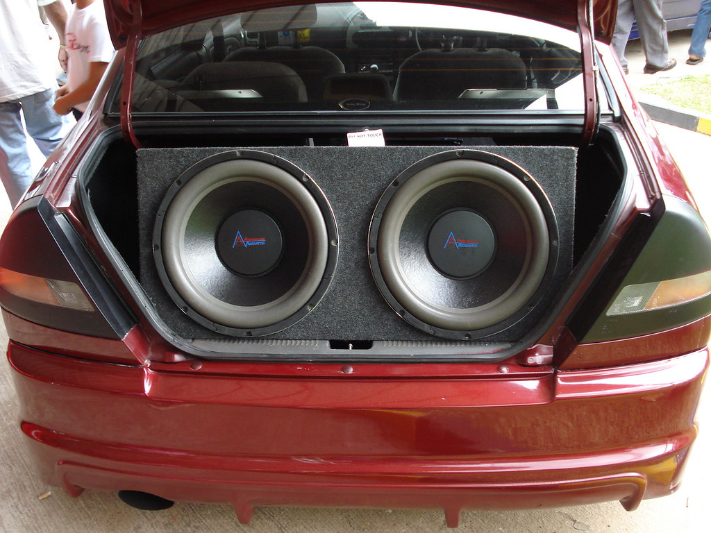 photo of the trunk of a small red car filled with two large, round audio speakers