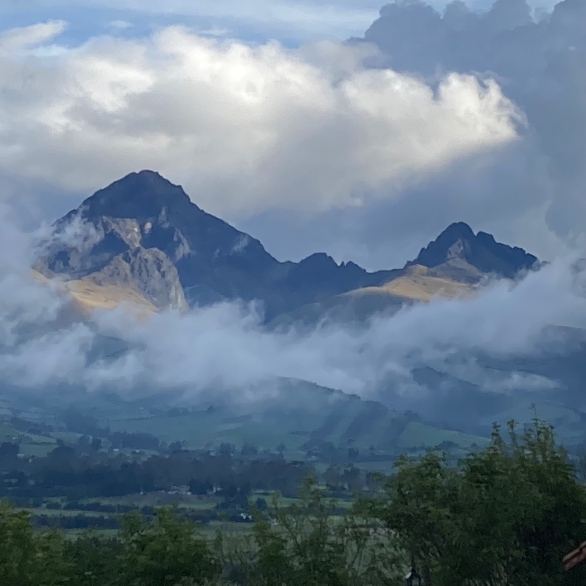 photo of a mountain ridge on the horizon, surrounded by clouds, with rolling green fields in the foreground