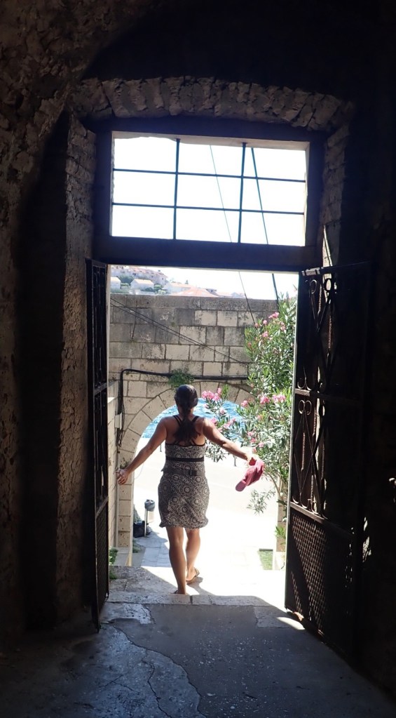 photo of a darkened doorway in a courtyard with a woman in a summer dress walking through into the light.