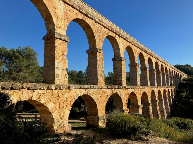 photo of a two-level structure of arches crossing a ravine with blue sky behind