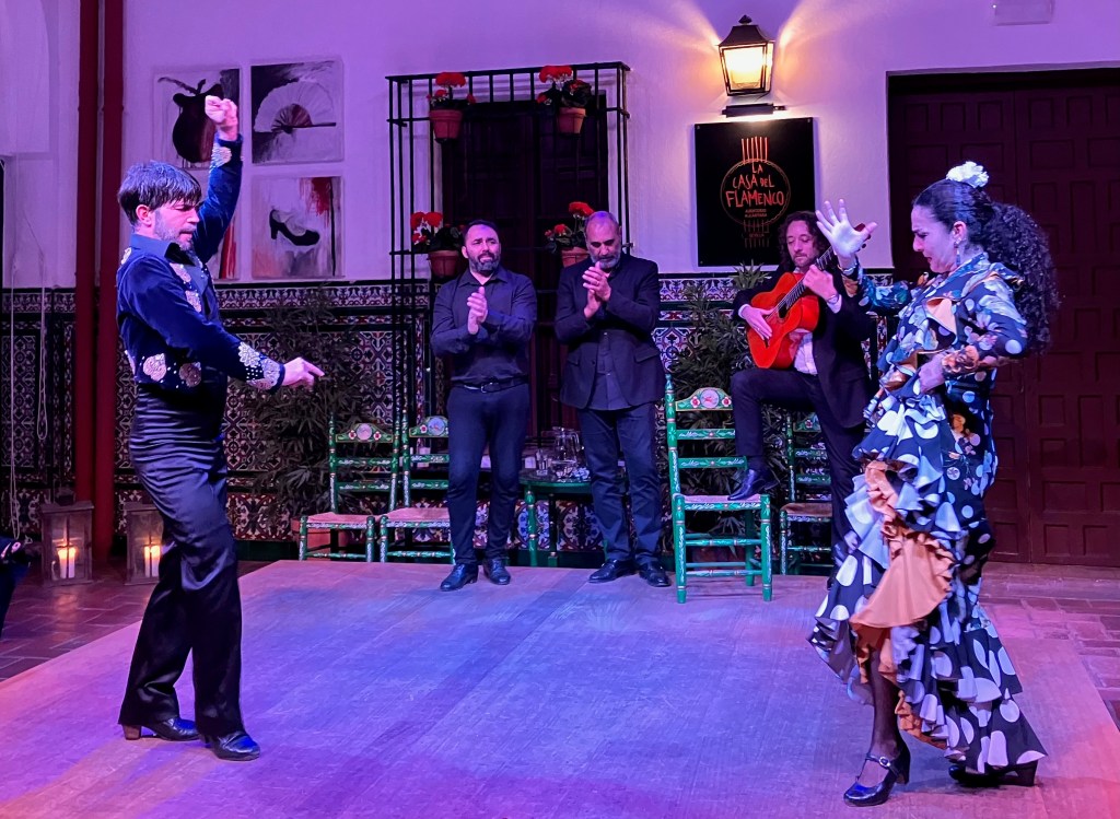 photo of a male and female flamenco dancer in the foreground with a male guitar player and two male singers clapping in the background.