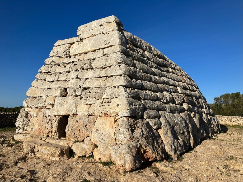 photo of a stone hut-shaped structure showing a flat front wall with a small opening and a sloped side wall.