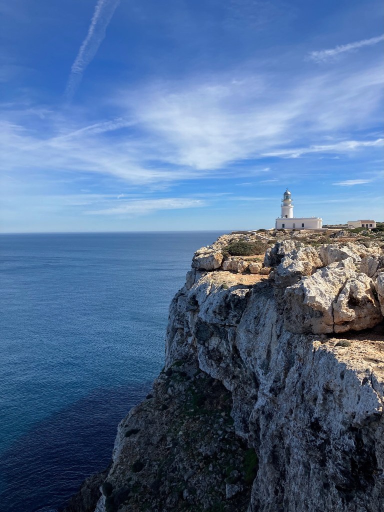 photo of steep white cliffs next to deep blue, wide sea with a lighthouse on the cliff