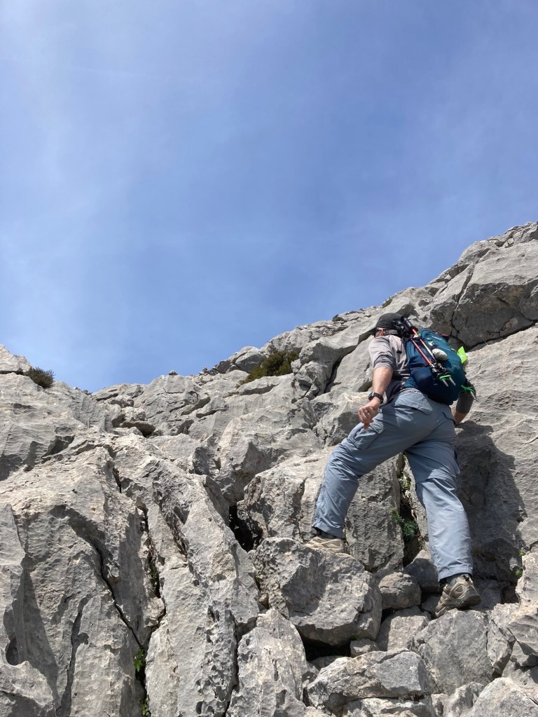 photo of a man climbing up a steep grade of gray boulders.