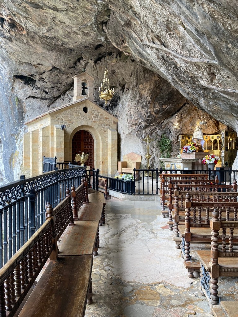 photo of a chapel set inside a rock cave, with wooden benches in the foreground