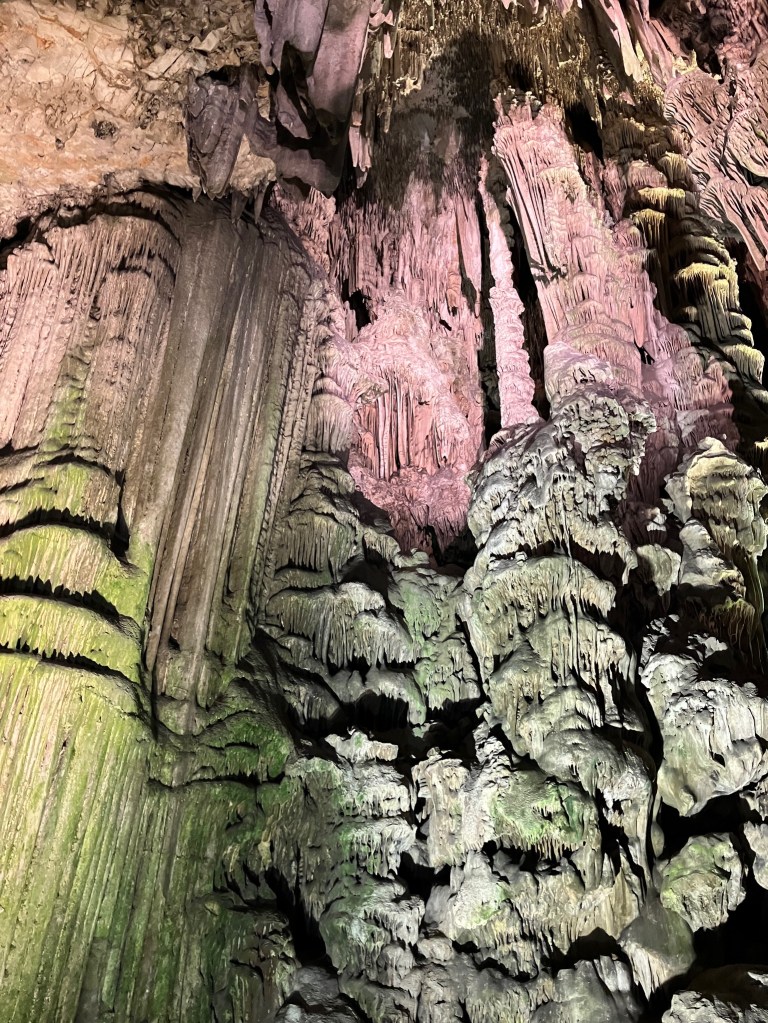 photo of towering stalactites in lit in green, pink, and gray