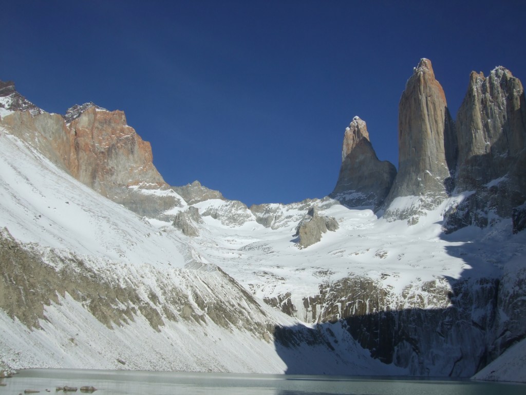 photo of Torres del Paine, three stone towers with snow caking the cliffs below them above a glacial lake