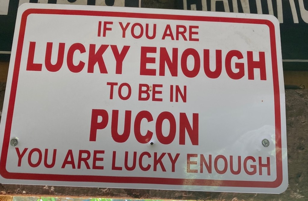 photo of a sign with red type on a white background. It reads IF YOU ARE LUCKY ENOUGH TO BE IN PUCON YOU ARE LUCKY ENOUGH.