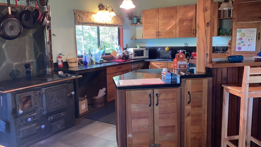 photo of a kitchen with wood cabinets, black granite counter, and large, cast-iron wood stove and oven with saucepans hanging over it