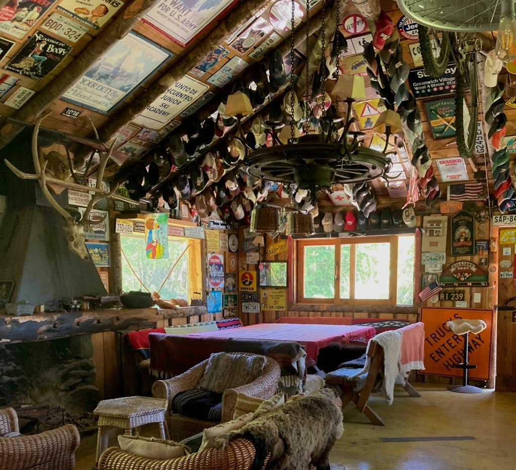 photo of a large room with a fireplace on the left wall, a few rattan chairs and a table with chairs for eating. All the walls and ceiling space are covered with posters, license plaes, hats, road signs, and memorabilia.
