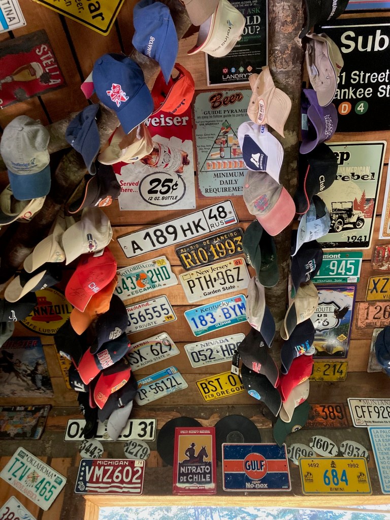 photo of a wooden ceiling covered with multicolored baseball caps, license plates, and old-fashioned placards.