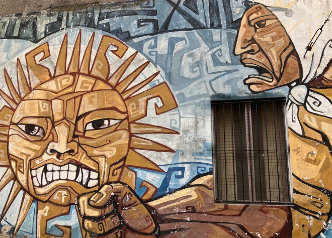 photo of a wall mural around a grated window depicting an angry woman with a white kerchief on her head shaking her fist at an angry sun