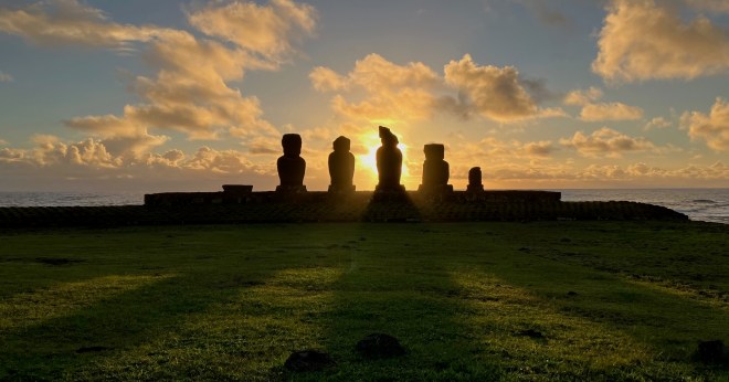 photo of five moai statues silhouetted against a bright yellow sunset and orange clouds
