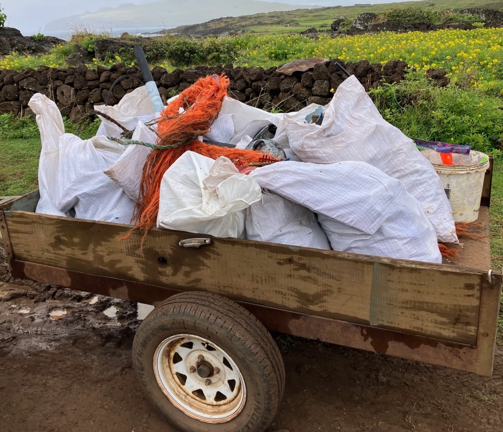 photo of a wagon containing 8 large white bags of trash and a large orange plastic rope on top