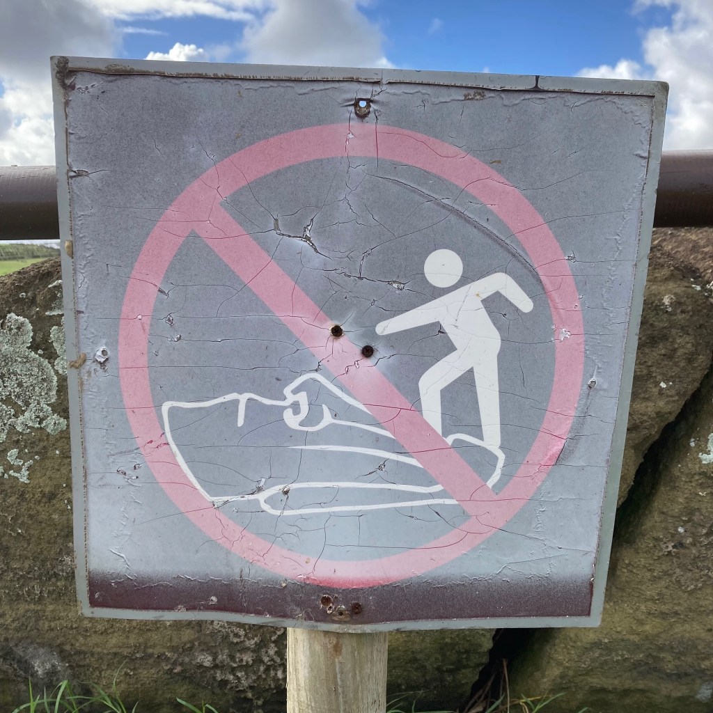 photo of a sign depicting an outline person stepping on an outline moai head and a red circle and slash over it