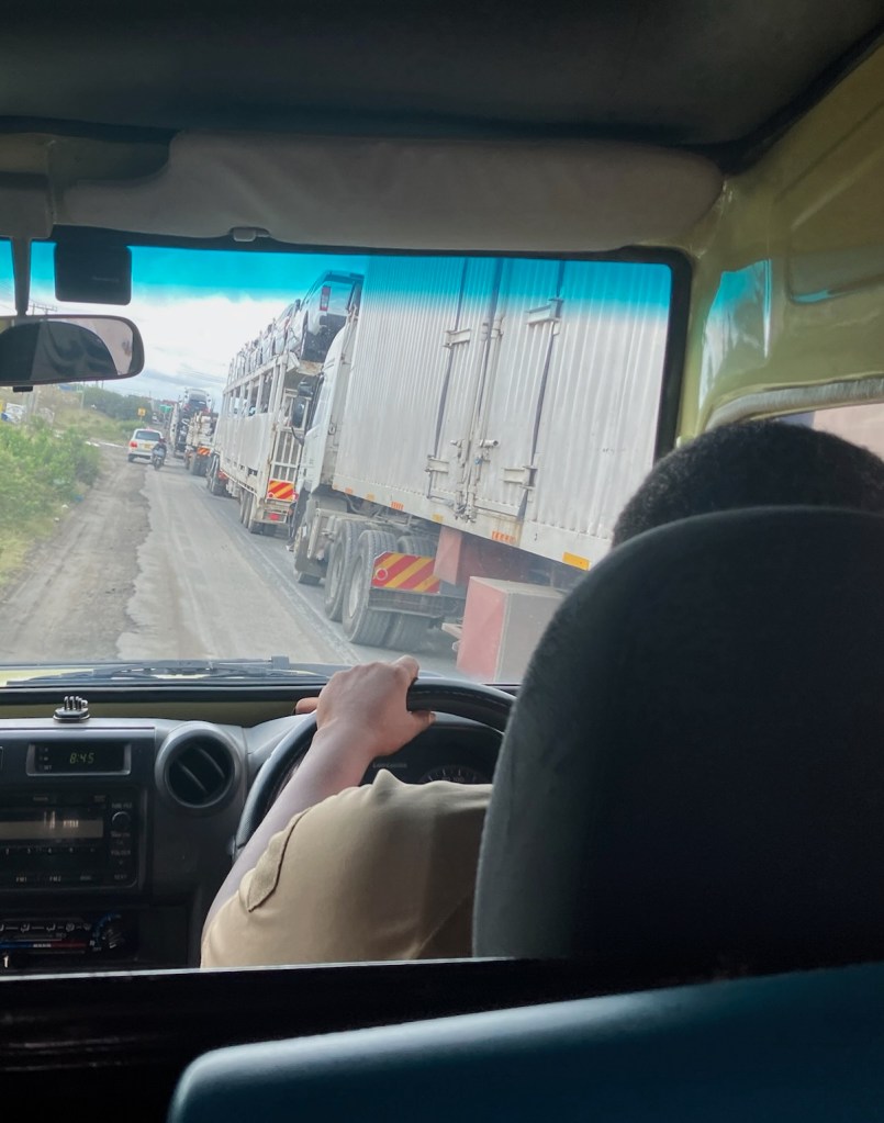 photo of a line of tractor trailer trucks taken from the back seat of a car driving on the roadside