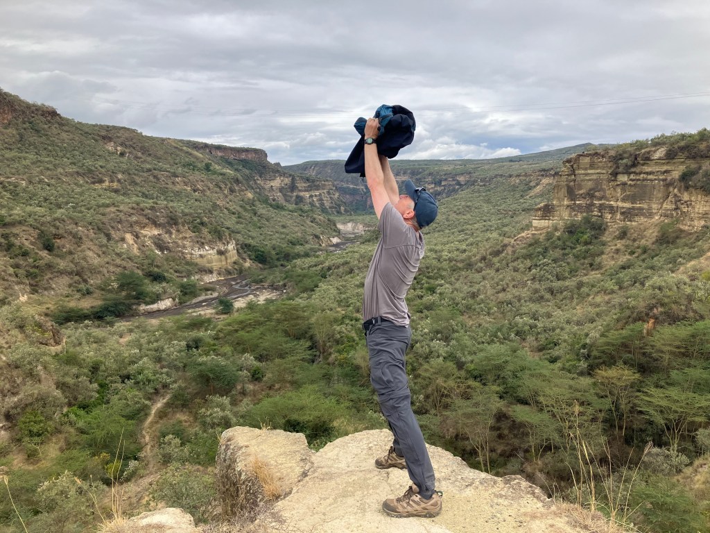 photo of a man standing on the edge of a stone overlooking a wide canyon, holding a bundle above his head