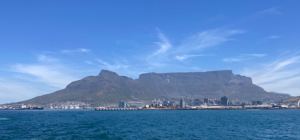 photo across water of flat-topped Table Mountain behind the tall buildings and wharf cranes of Cape Town