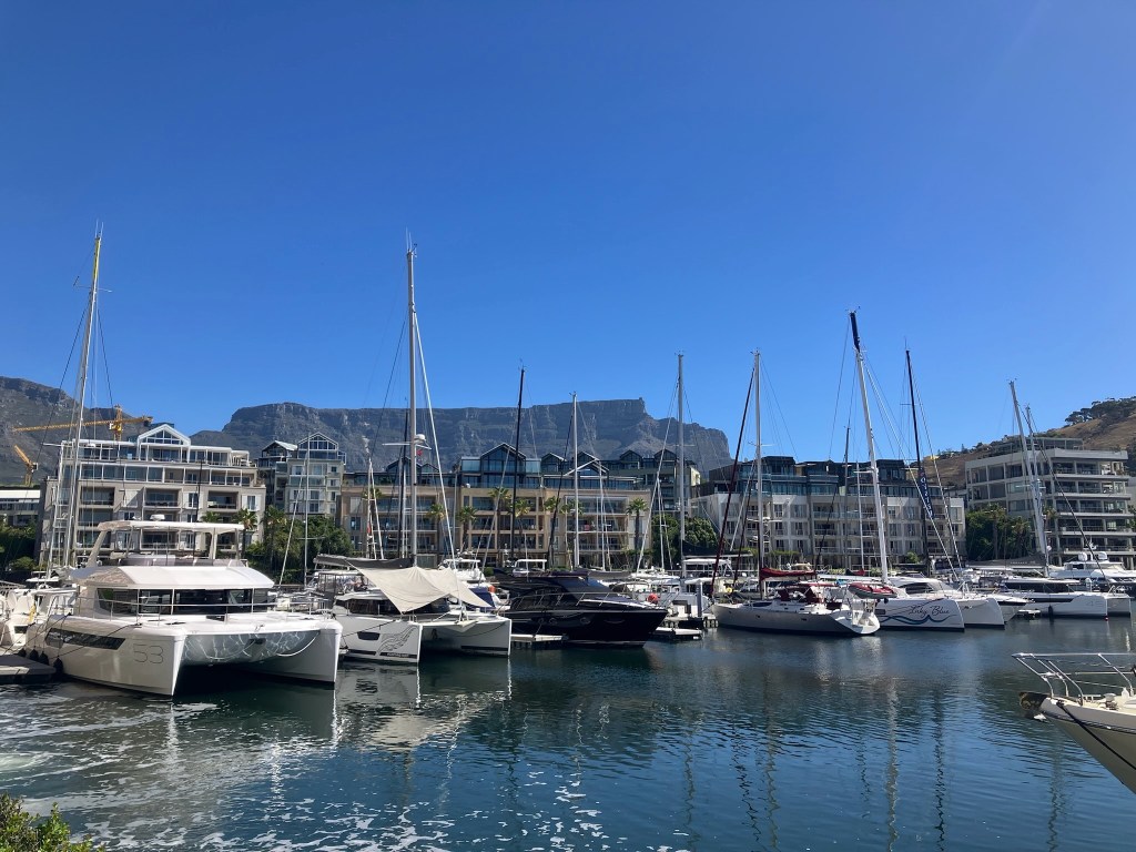 photo of large sailboats in a placid harbor with white, 6-story condos behind, and a flat-topped mountain behind them