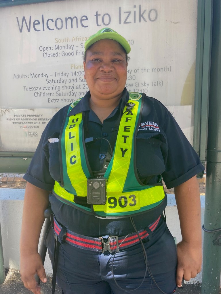 photo of a smiling security guard wearing a blue uniform and neon yellow belt that says Public Safety