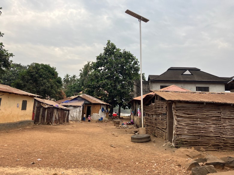 photo of a brown dirt road with single-story houses made of sticks and cinder blocks on either side