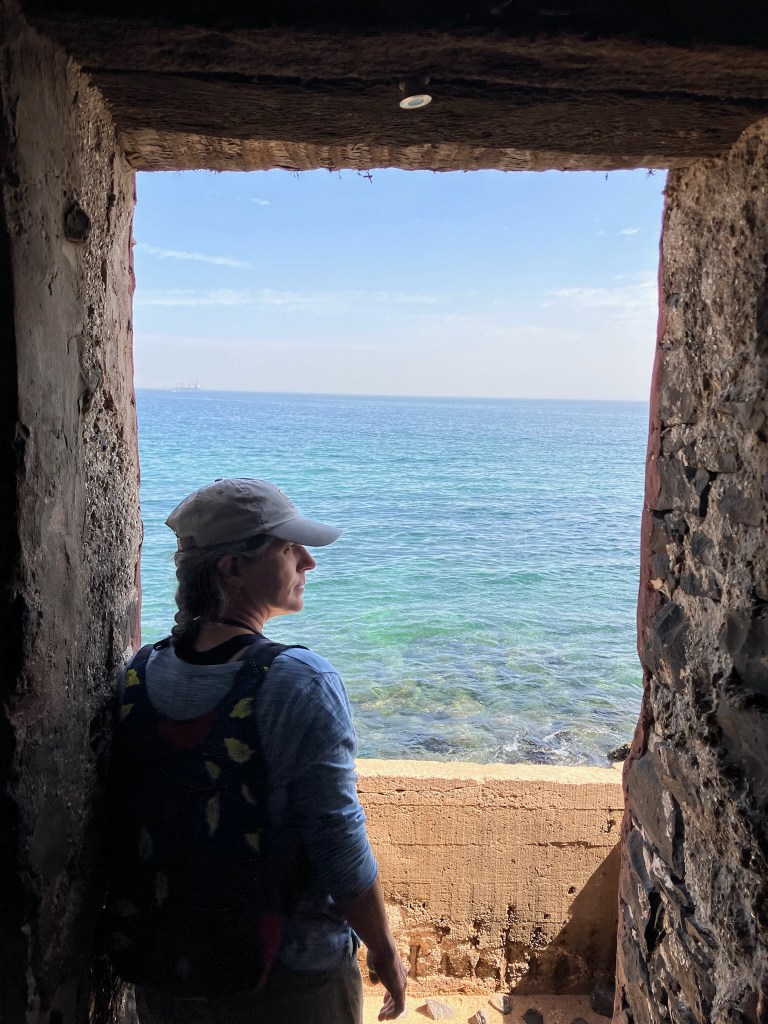 photo of a woman in a baseball cap looking pensively across blue-green water, framed by a stone doorway