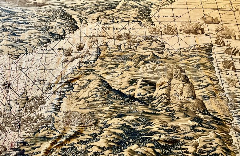 Light brown and black antique map with captions in Spanish, showing mountains in the foreground and background, with the Mediterranean Sea between and sailing ships squeezing through the Gibraltar Strait.