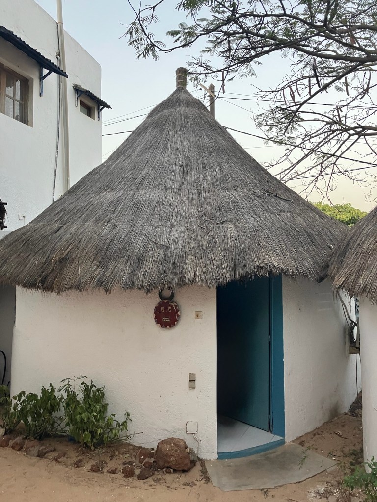 photo of a small white circular cement hut with a conical gray thatched grass roof