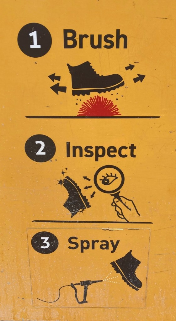 Image of a yellow sign saying (1) Brush (2) Inspect (3) Spray and drawings depicting a boot going through the steps.