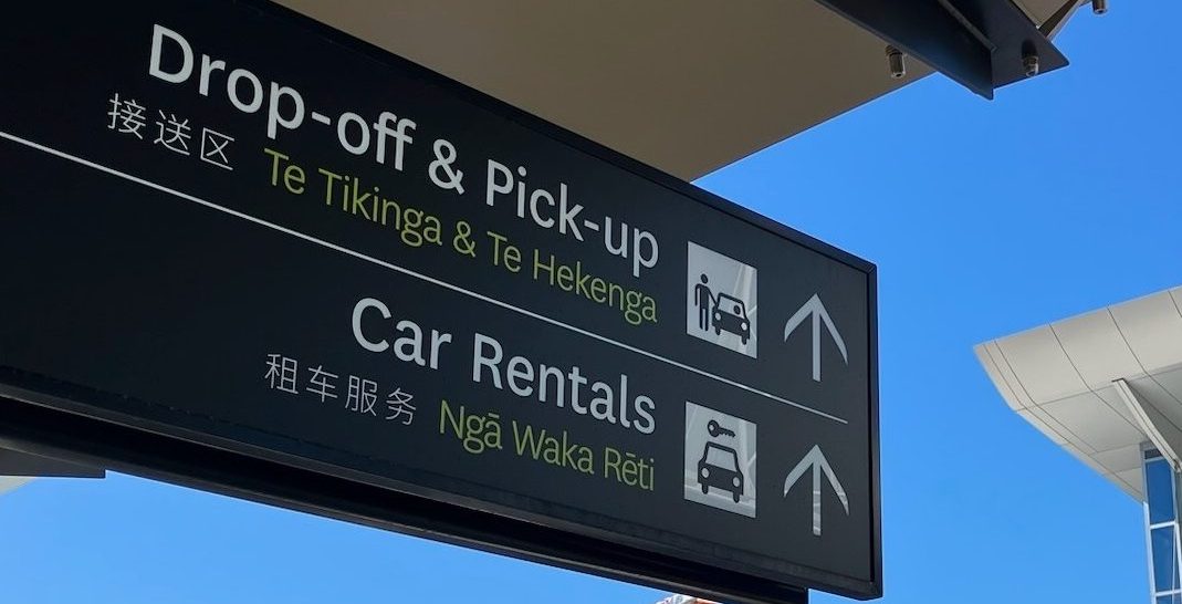 photo of airport signs for Drop-off and Pickup and Car Rentals with Japanese and Maori translations beneath.