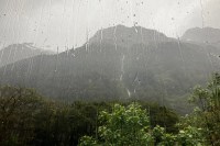 photo through a rain-streaked window showsing leafy green trees in front of blurry dark green mountains