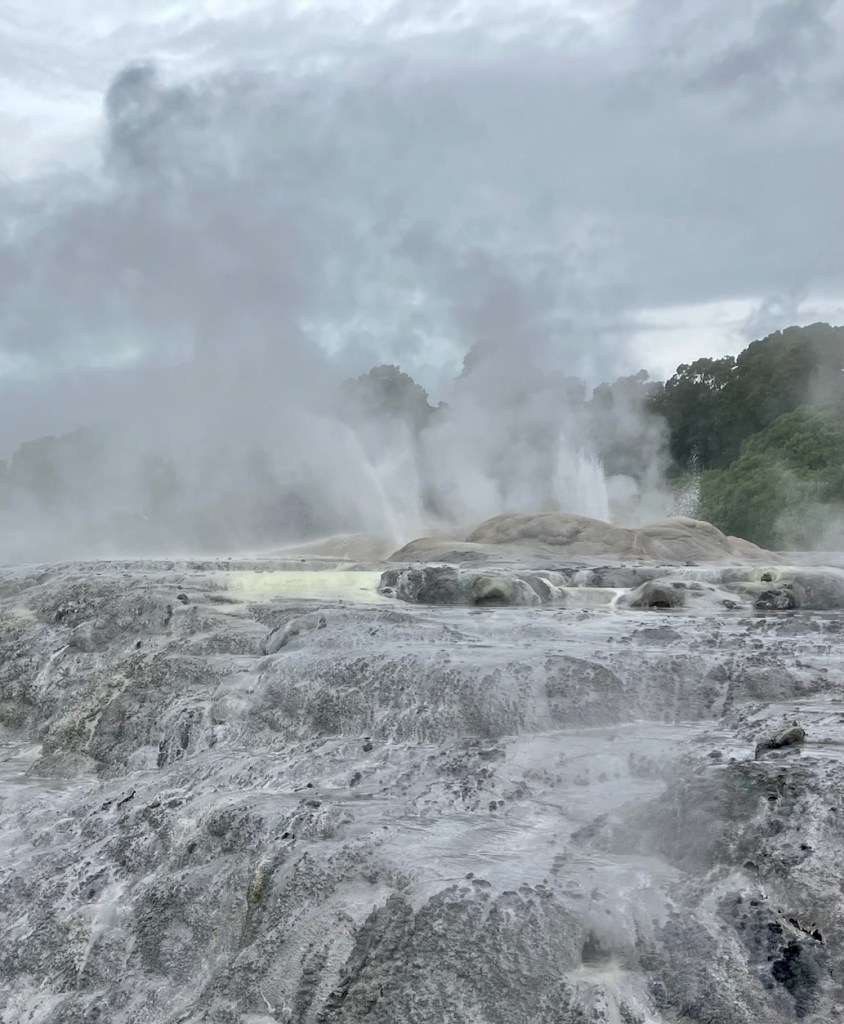 photo of water spouting and spraying up from brown rocks covered with white silica and a cloudy sky in the background