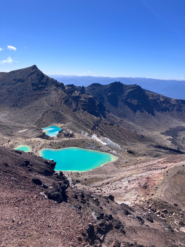 photo of three blue-green ponds amidst a barren, rocky, brown landscape with jagged brown mountains behind them and a deep blue sky above