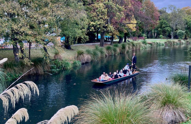 photo of a low, flat, green boat in a dark river with 9 passengers and one person standing in the back and holding a pole