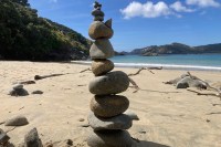 photo of a cairn of 12 rocks balanced precariously on the sand with blue-green water in the background