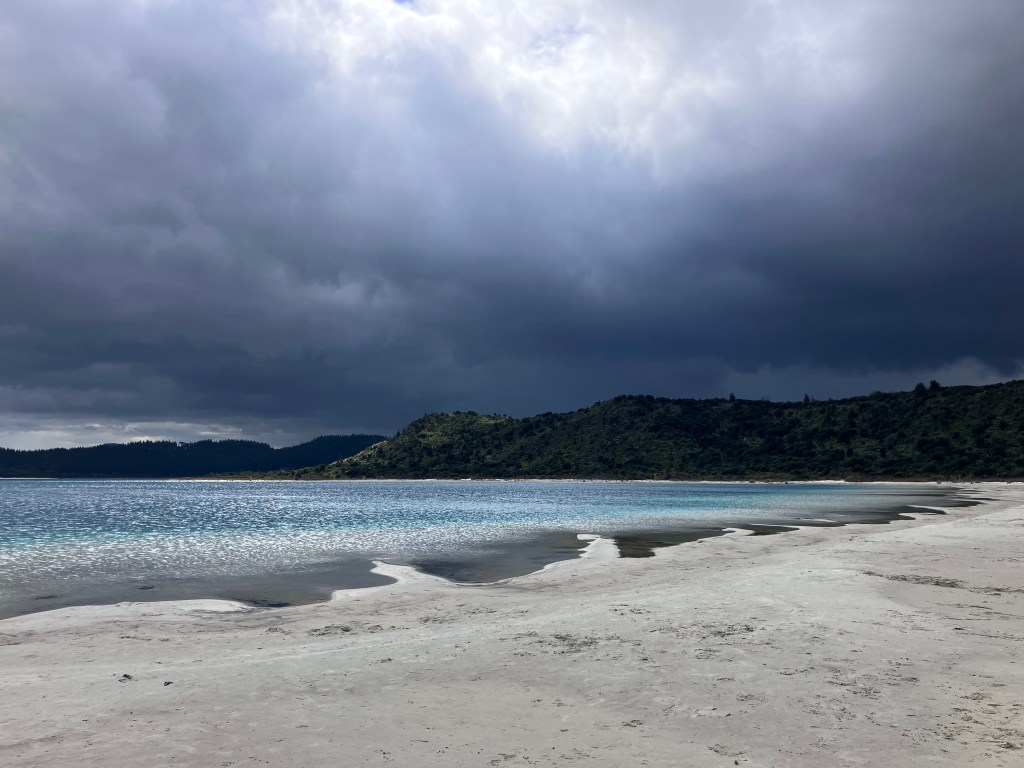 photo of a wide, empty, white-sand beach glittering in the sun with dark clouds looming in the distance
